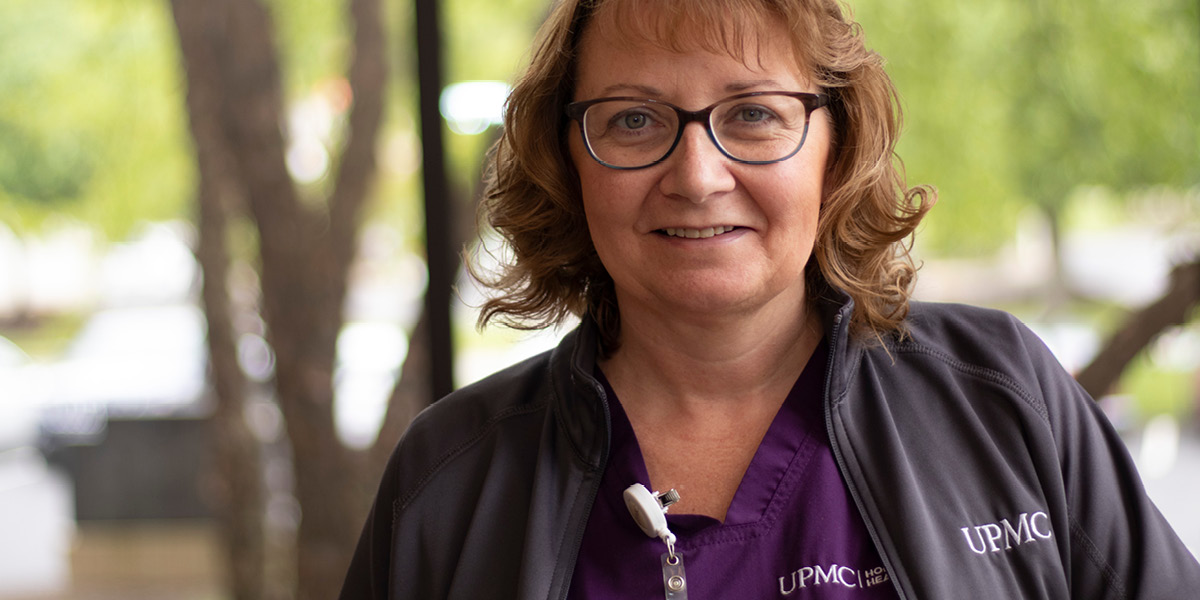 Woman wearing UPMC scrubs smiling with trees in the background
